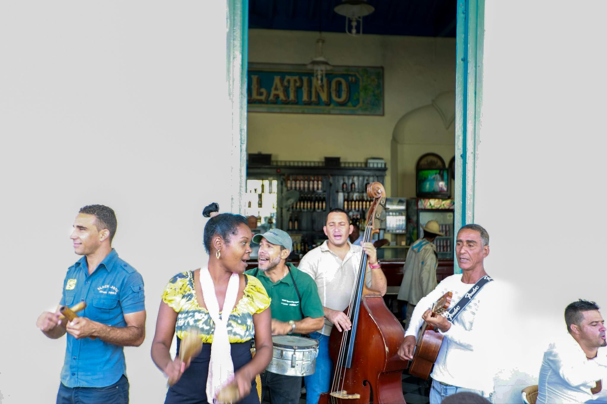 Street musicians performing lively music with guitars, maracas, and more outside a Latin bar.